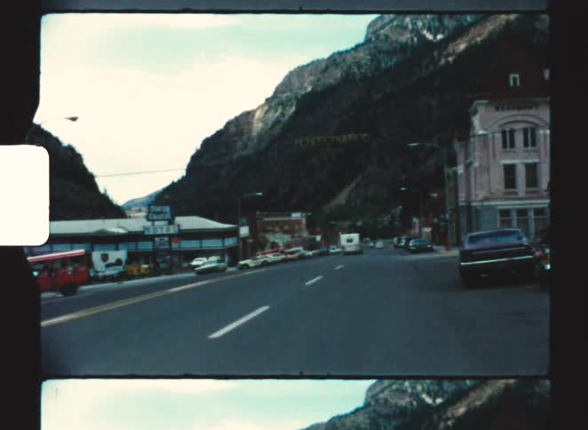 Main street of a mountain town with parked vehicles and shops along the road