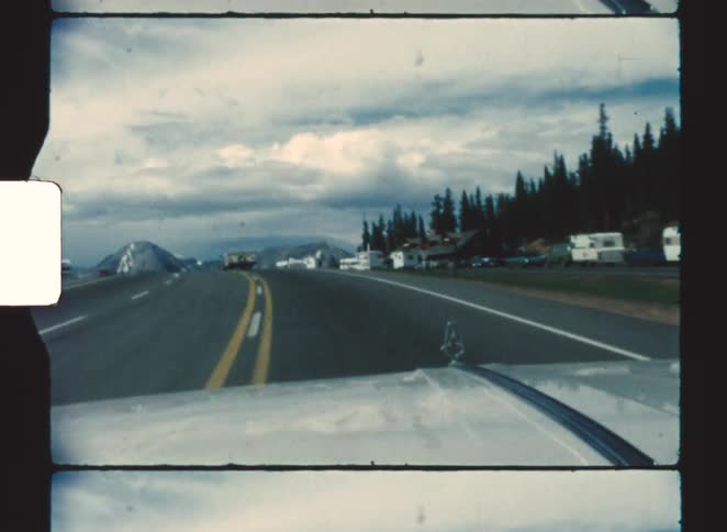 Road seen from inside a car with double yellow lines vehicles ahead and trees lining the route
