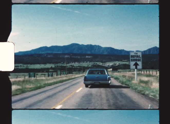 A sedan driving along a countryside freeway at midday passing a road sign that reads royal gorge