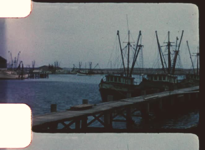 Fishing boats moored at wooden dock with maritime structures in background