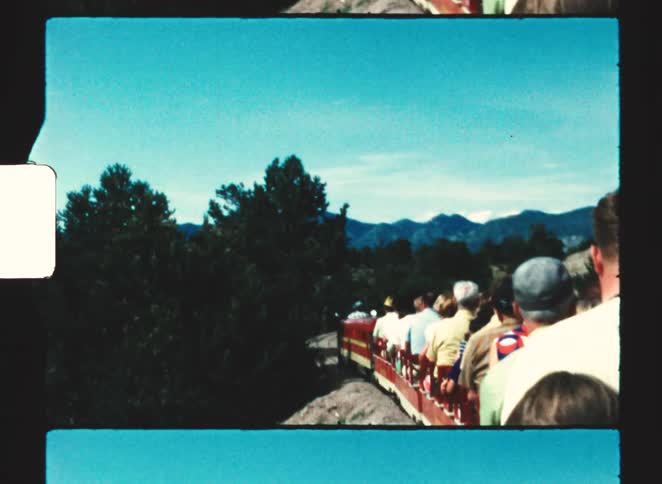 Red train with yellow stripes carrying people along curved track in wooded area