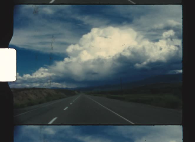 Rural highway passes fields and hills on a cloudy day