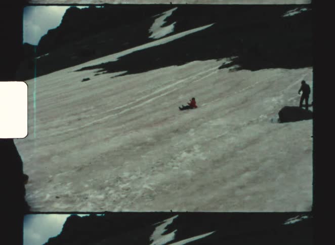 Children play in snow on mountain slope wearing winter clothing