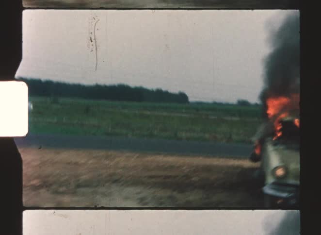 The car is in flames on the side of the highway