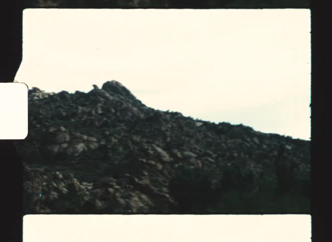 Rocky slope displays uneven terrain with scattered boulders under clear sky