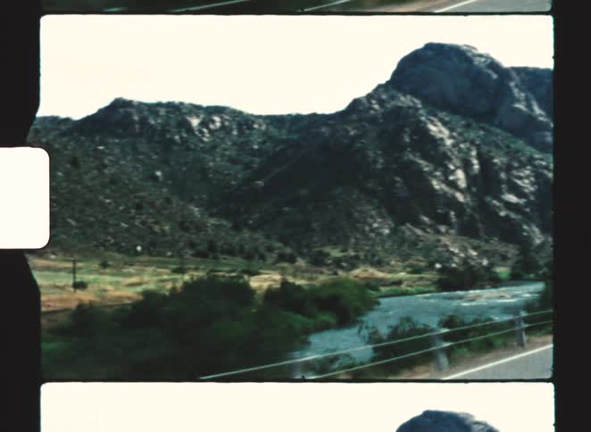 A winding river flows past rocky mountains and green vegetation in a wide landscape
