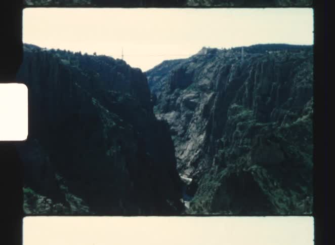 A narrow canyon with steep dark rock walls under a bright sky