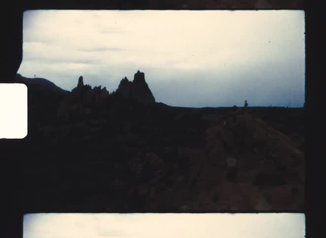 Jagged rock formations rising under cloudy sky in dark terrain