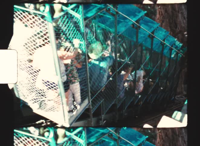 A cage like funicular car filled with passengers moves down a steep incline alongside a rocky canyon wall