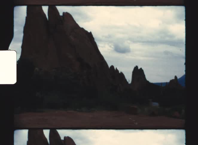 A car parked on the side of a rocky mountain with a pointed peak illuminated by the warm colors of sunset