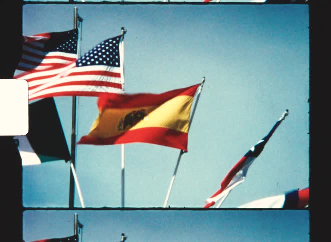 A series of flagsincluding two american flags one spanish flag and several othersfluttering in the wind at midday