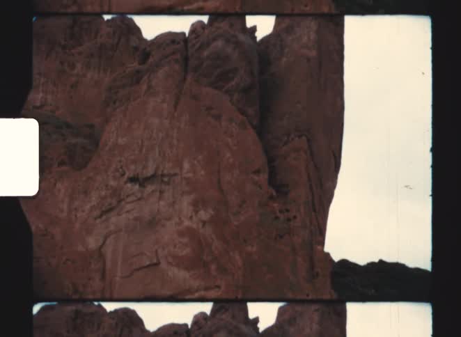 Two vehicles sit parked near the base of a red rock formation on a cloudy summer day