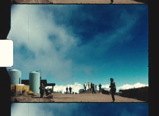 A group of people stand on a high mountain observation deck under a vast bright blue sky with wispy clouds