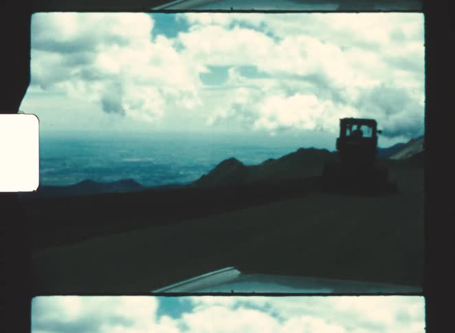A vehicle travels along a coastal road beneath cloudy skies