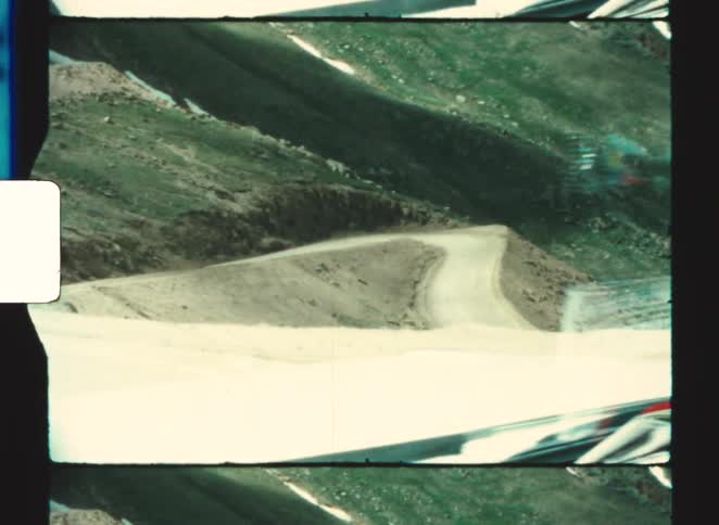 A car driving through the countryside at midday passing a hill covered in lush green vegetation