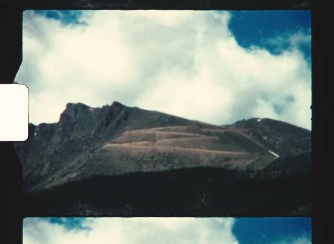 pikes peak Rocky slope with sparse vegetation beneath blue sky filled with voluminous clouds