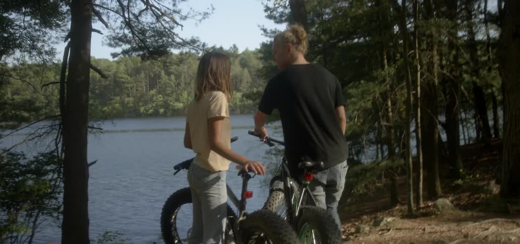 Man and woman standing with bikes and talking next to forest lake