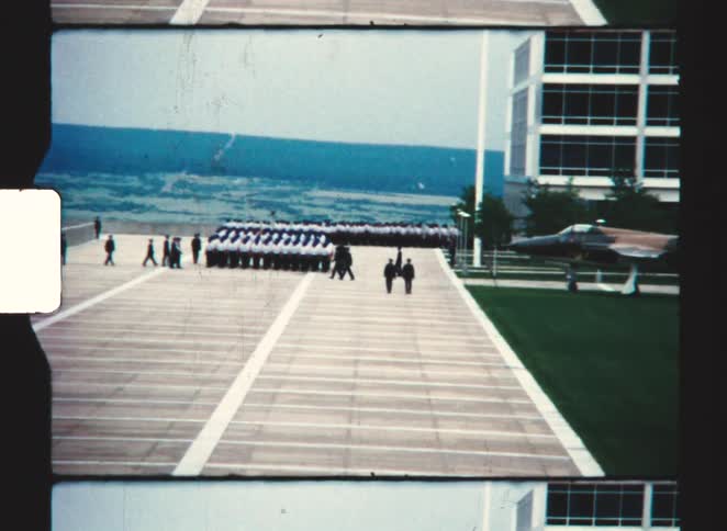 Uniformed group in ceremonial formation near displayed jet beside modern building overlooking valley