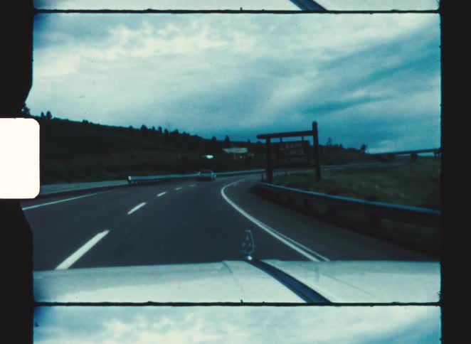 Curving road seen from inside a car with white lane markings vehicles ahead and a cloudy sky