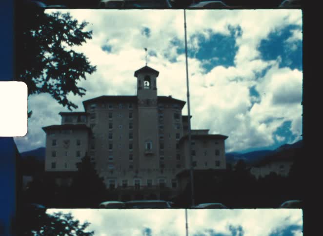 the broadmoor hotel colorado springs 1970 An imposing historic building with a prominent central tower seen down a street lined with parked cars