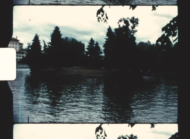 A lake surrounded by trees with a building on the far side in the background at sunset