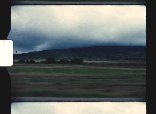 A car driving through the countryside with powerlines running along the grassy roadside under a cloudy midday sky
