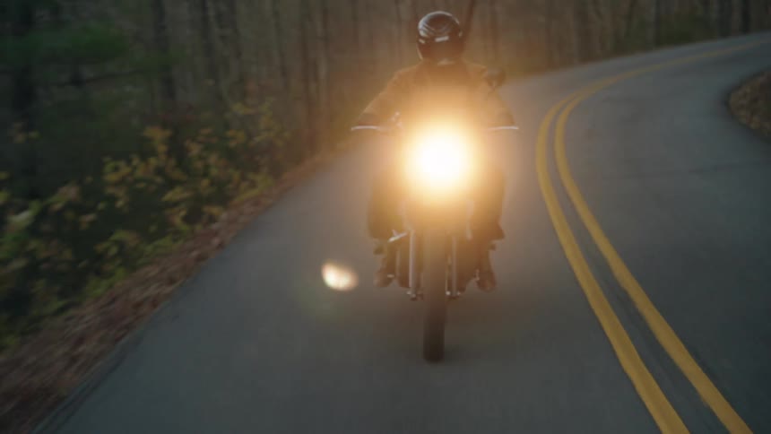 Motorcyclist rides along a winding road with headlight on and yellow center lines