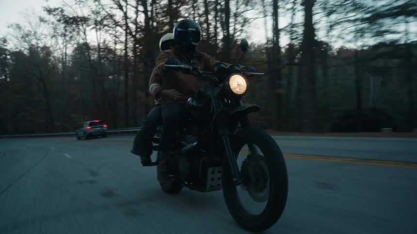 A couple riding a motorcycle along a forest road at dusk