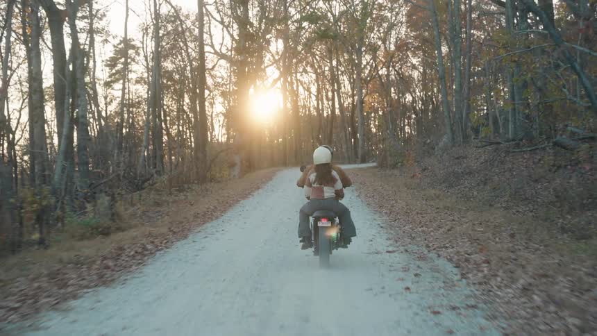 Couple on a motorcycle riding along a dirt road surrounded by forest