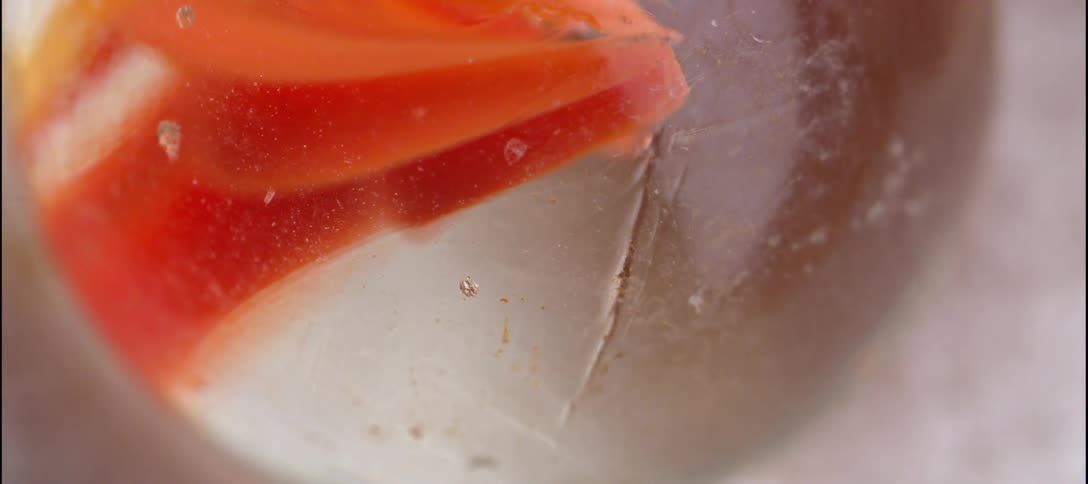 Glass marble with orange internal bands and a translucent surface in closeup