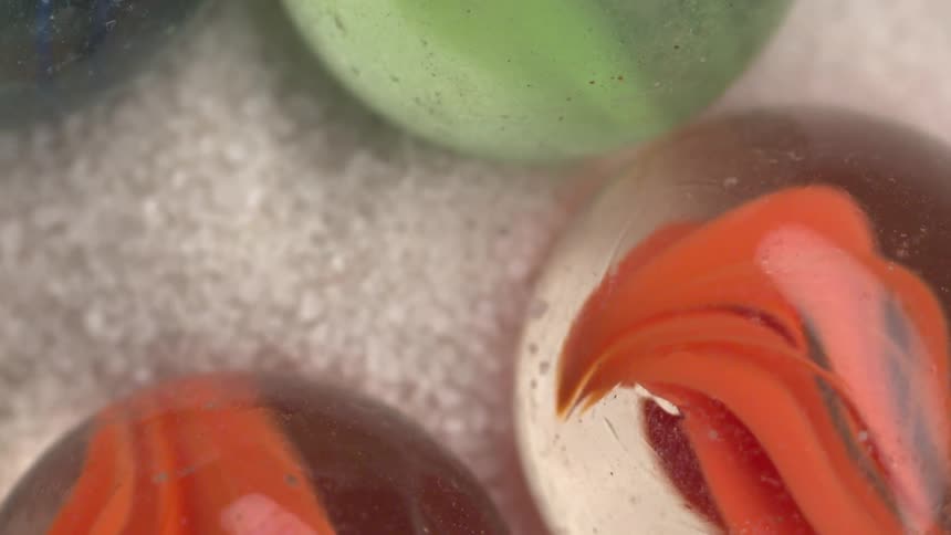 Colored marbles with internal patterns rest on a light granular surface