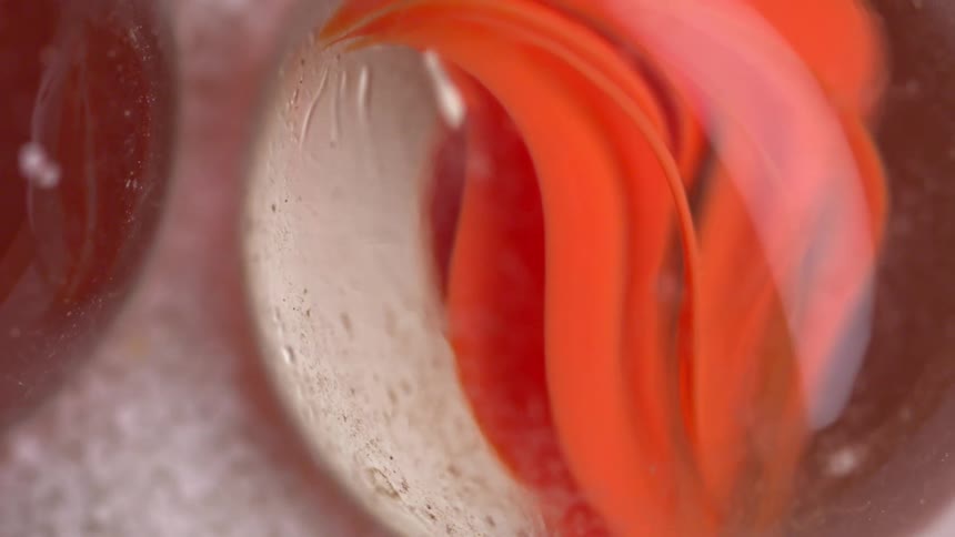 Marbles with red and light patterns appear in closeup on a granular surface