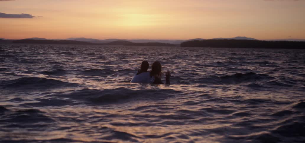Two people float in the water together at sunset