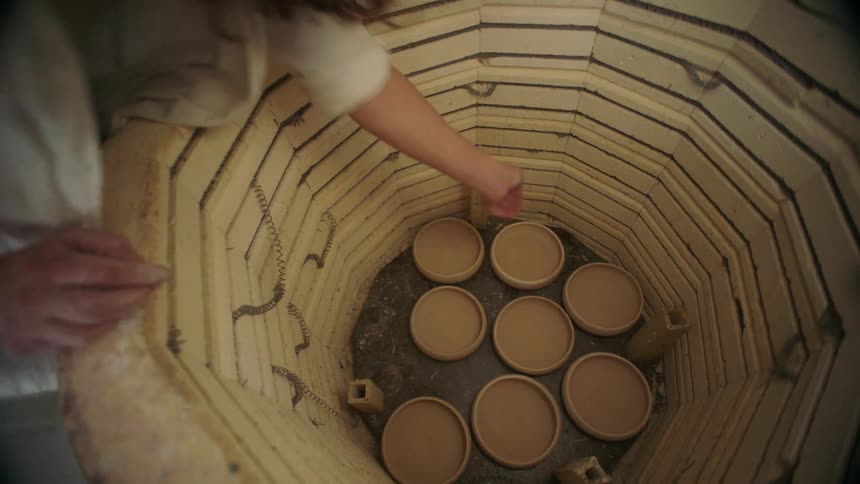 A woman placing a ceramic vase inside a huge container with several others