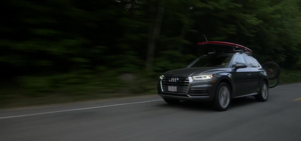 A car with a surfboard on top travels on the road