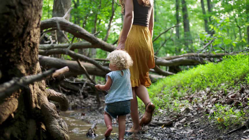 A blonde little girl walking in a puddle of water while holding a hand with an adult