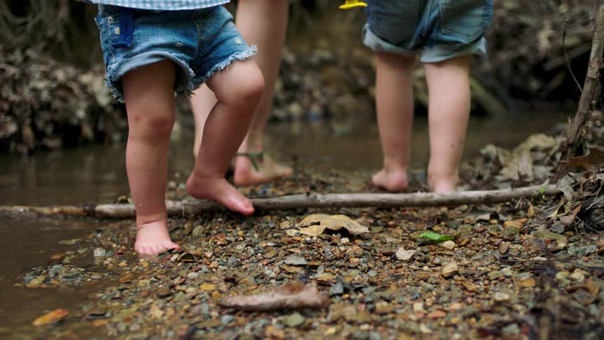 Woman and her kids walk through and near a stream barefoot on a summer day