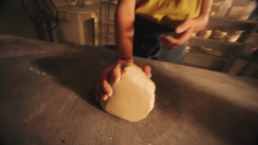 A woman places an unshaped mound of clay onto a counter