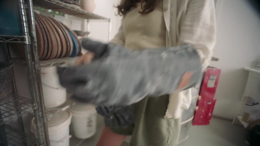 A young woman picking up a pair of gloves from a shelf indoors at midday getting ready to start cleaning