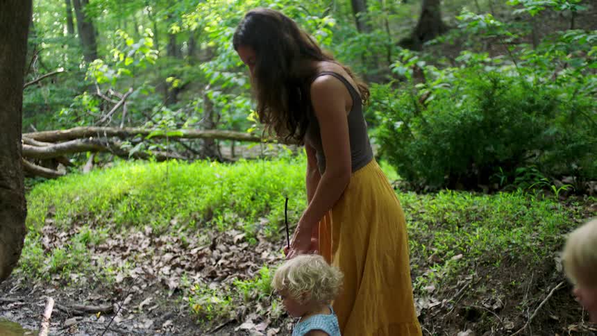 Woman standing in a forest with two young children surrounded by green vegetation