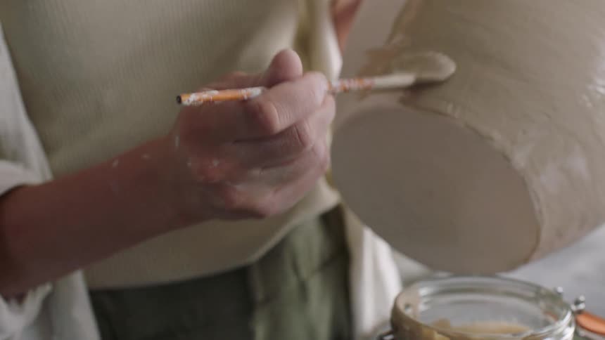 Hands hold and refine an unfired ceramic piece during the shaping process
