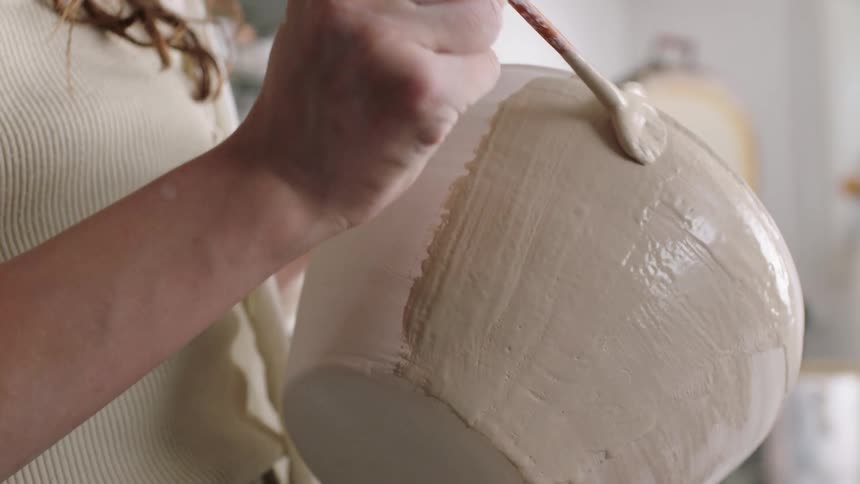 Woman holds a paint brush as she paints a ceramic bowl