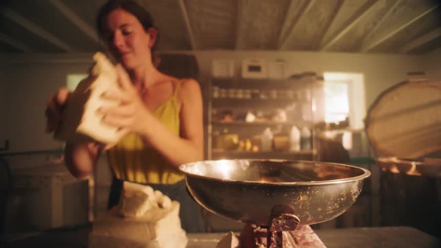 Woman picks up clay from a metal scale inside a studio with natural lighting