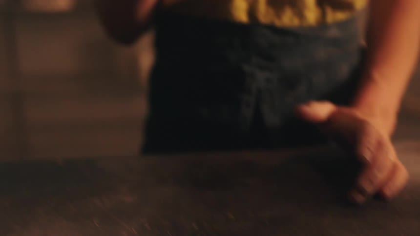 Female hands shaping a lump of clay and beating it against a table indoors
