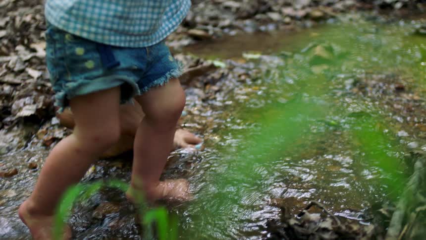 Woman walks barefoot through a shallow stream with her child on a summer day