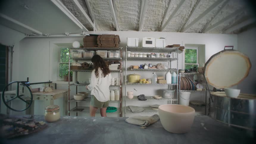 Ceramicist walks through the studio and places a ceramic piece between shelves