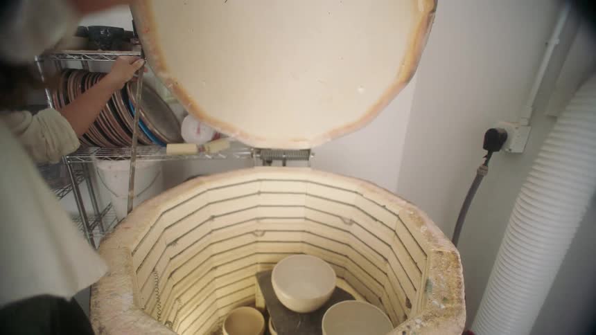 Female potter removes a bowl from a kiln in her workshop