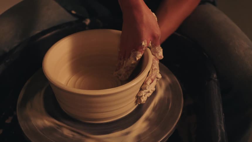Hands shaping clay bowl on pottery wheel in crafting process
