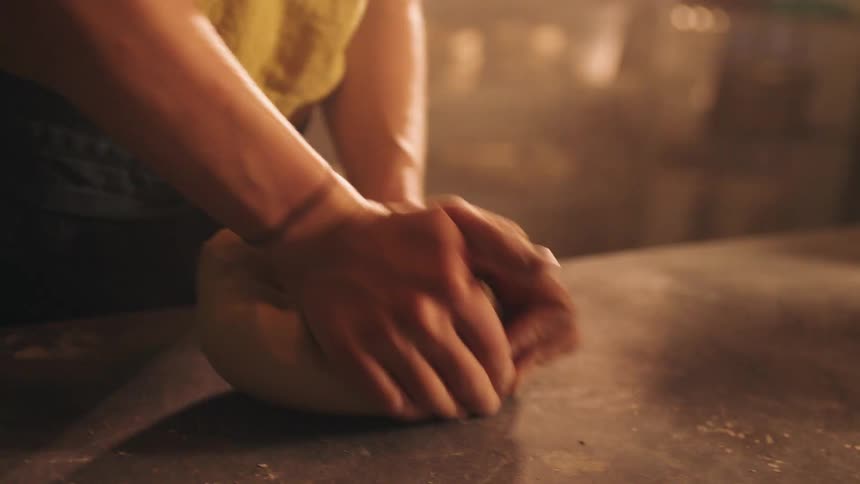 Young female hands kneading a piece of clay indoors over a table