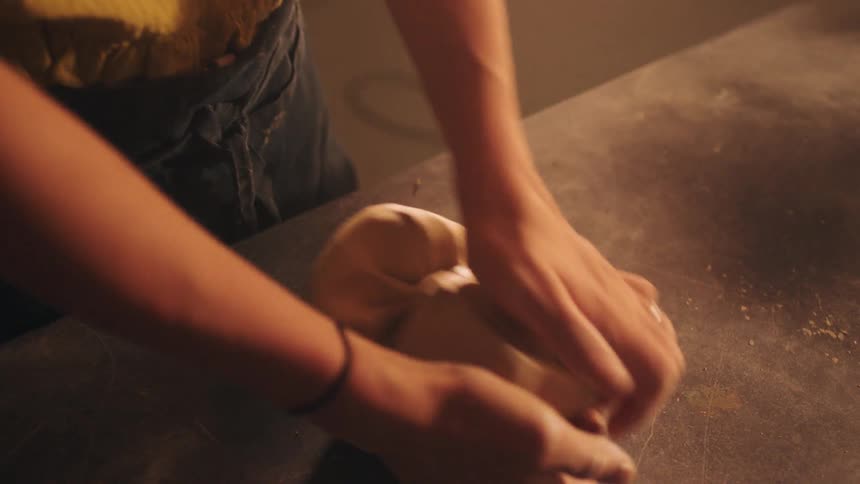 Hands press and rotate a portion of clay on a work surface
